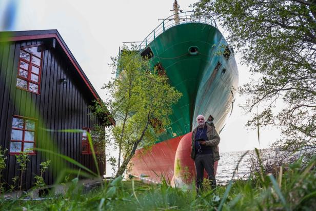 Ein Mann steht vor einem großen, gestrandeten Schiff in Norwegen.