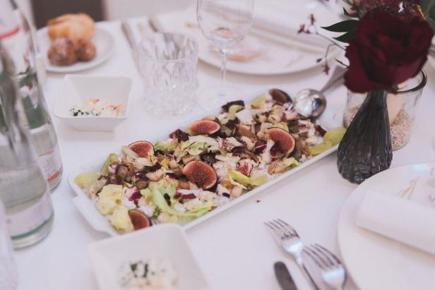 Ein Tisch ist mit einem Salat mit Feigen, Besteck und Getränken gedeckt.