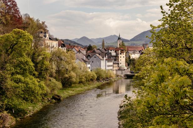Eine malerische Stadt liegt an einem Fluss, im Hintergrund sind Berge zu sehen.