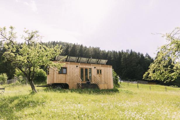 Ein hölzernes Tiny House mit Solaranlage steht auf einer grünen Wiese.