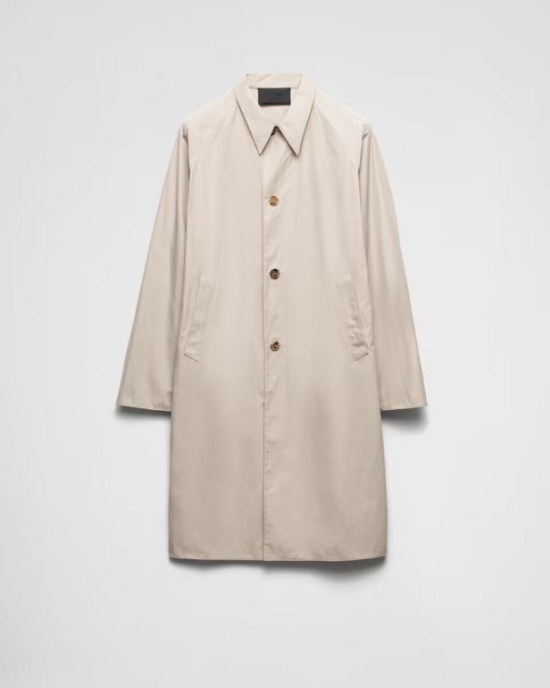 Ein beigefarbener Trenchcoat hängt vor einem weißen Hintergrund.