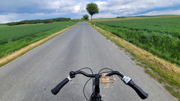 Das Lenkrad eines Fahrrads, eine Landstraße und Felder an den Seiten.