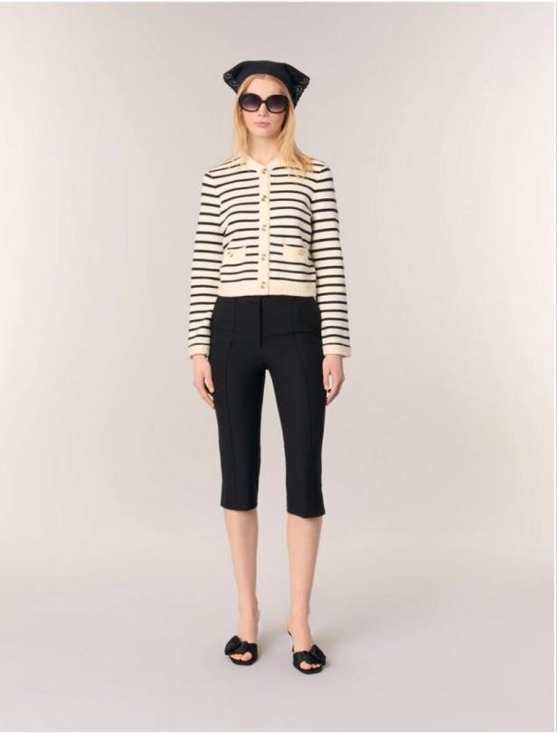 Eine Frau mit Sonnenbrille, Kopftuch, gestreifter Strickjacke und schwarzen Caprihosen.