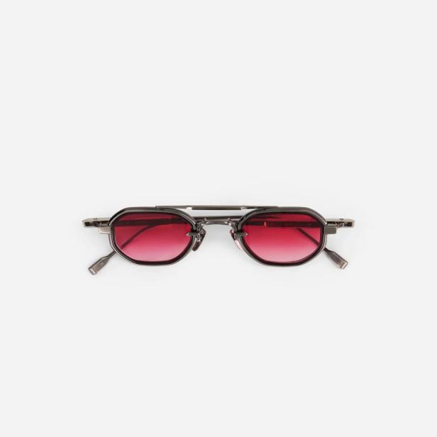 Eine achteckige Sonnenbrille mit rot getönten Gläsern liegt auf einem weißen Hintergrund.