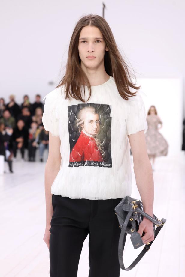 Ein Model auf dem Laufsteg mit einem T-Shirt mit dem Aufdruck „Wolfgang Amadeus Mozart“ und einer Handtasche von Loewe.