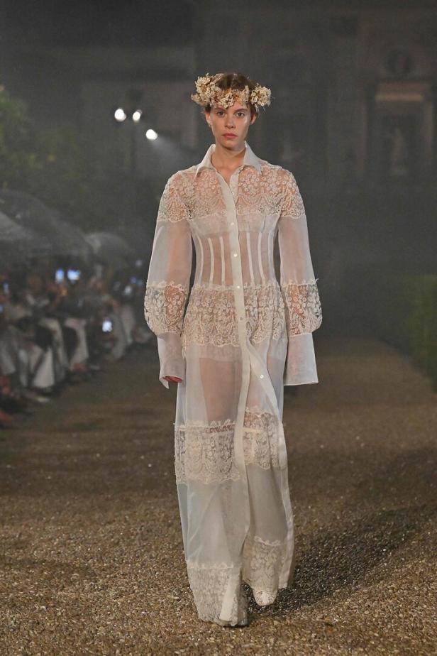 Eine Frau mit Blumenkranz trägt ein transparentes, weißes Kleid mit Spitze auf einer Modenschau in Rom.
