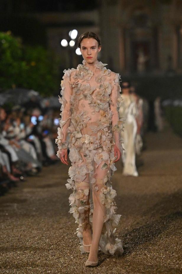 Ein Model präsentiert ein transparentes, mit Blütenblättern verziertes Kleid auf einer Modenschau in Rom.