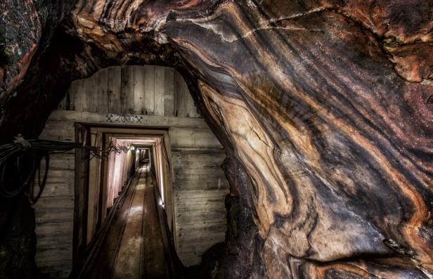 Ein Tunnel in einem Bergwerk mit farbigen Gesteinsschichten und hölzernen Stützbalken.