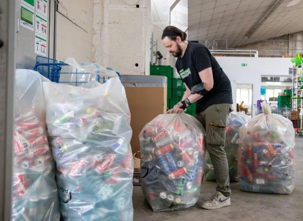 Alfies-Mitarbeiter trägt die gefüllten Säcke mit Pfandgut durchs Lager