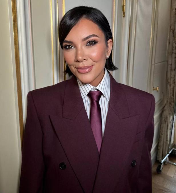Kris Jenner trägt einen dunkelroten Anzug mit Krawatte.