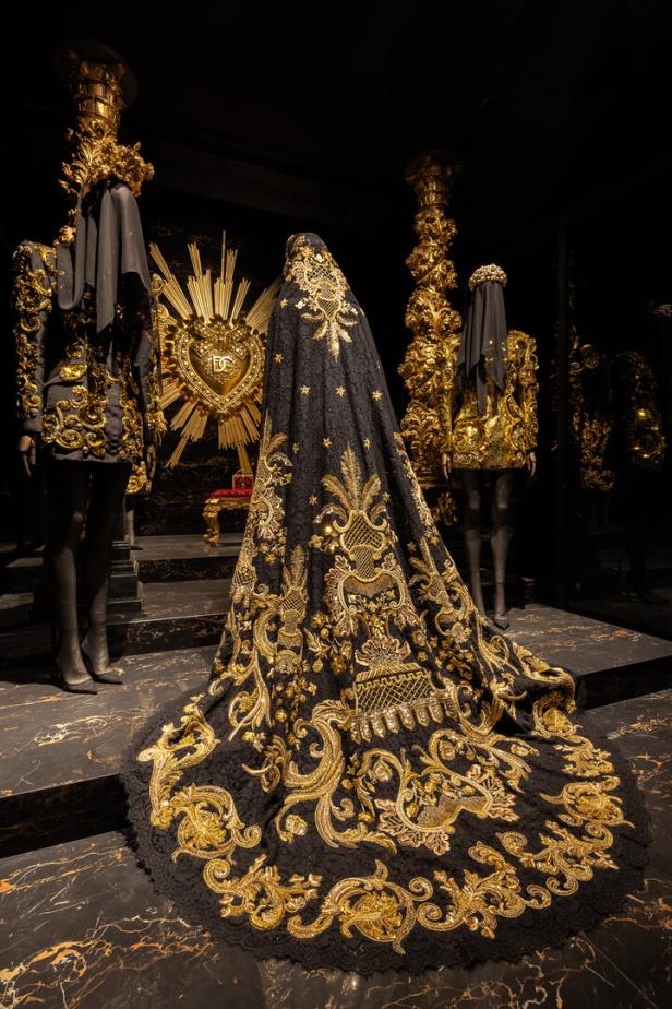 Eine schwarze Robe mit goldener Stickerei wird auf einer Modenschau präsentiert.