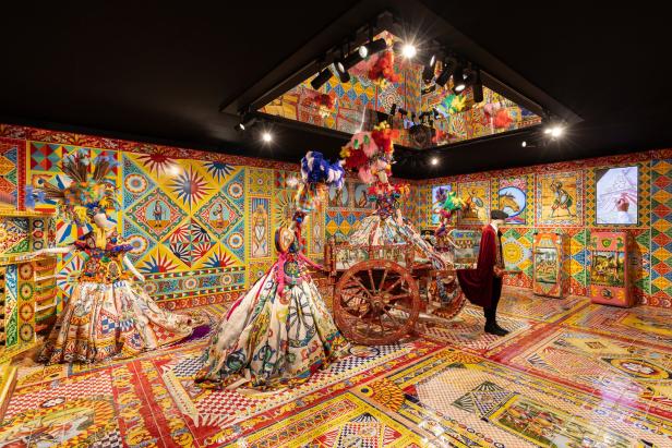 Ein Ausstellungsraum mit farbenfrohen, traditionell gemusterten Kleidern und einem Karren.