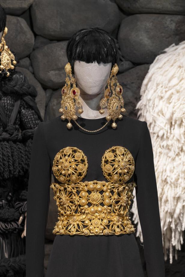 Eine Schaufensterpuppe trägt ein schwarzes Kleid mit goldenen Verzierungen und auffälligen goldenen Ohrringen.