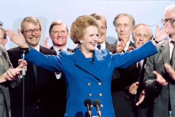 Margaret Thatcher jubelt mit erhobenen Armen vor einer Gruppe applaudierender Männer.