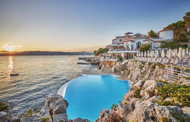 Ein Hotel mit Infinity-Pool liegt auf einer Klippe am Meer bei Sonnenuntergang.