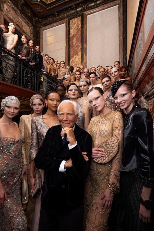 Giorgio Armani posiert mit einer Gruppe von Models auf einer Marmortreppe.