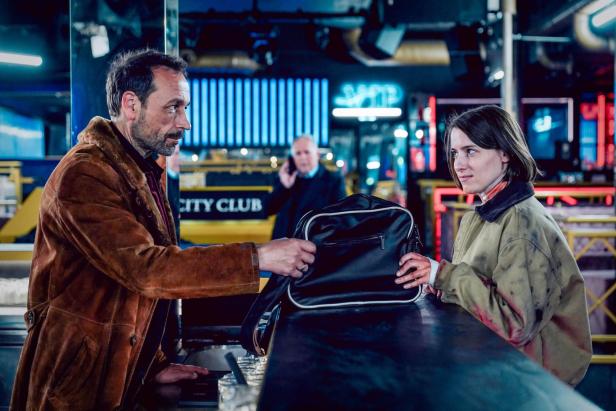 Szene aus „Tatort“: Ein Mann übergibt einer Frau eine Tasche an einer Bar.