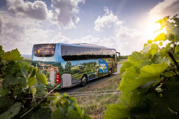 Ein Bus mit Werbung für das Burgenland fährt durch eine ländliche Gegend.