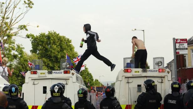 Ein Mann springt mit einer Flasche in der Hand über zwei Polizeiwagen.
