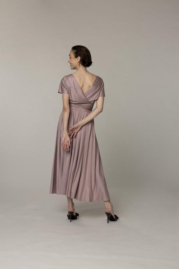 Eine Frau von hinten in einem altrosafarbenen Kleid und schwarzen Schuhen.