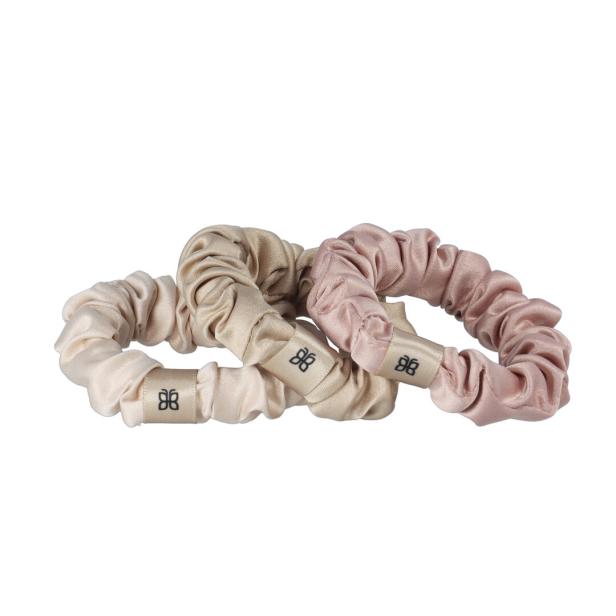 Drei Scrunchies in Beige- und Rosatönen liegen nebeneinander.