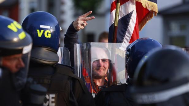 Ein Demonstrant hinter einem Schutzschild zeigt das Friedenszeichen, umgeben von Polizisten.