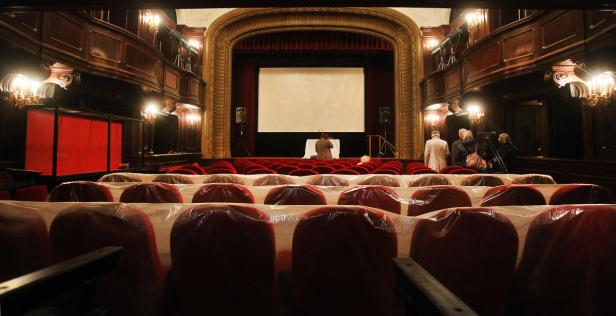Blick auf die Bühne eines Theaters mit roten Sitzen, die teilweise mit Plastik abgedeckt sind.