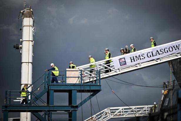 Arbeiter betreten die HMS Glasgow über eine Gangway vor einem dunklen Himmel.