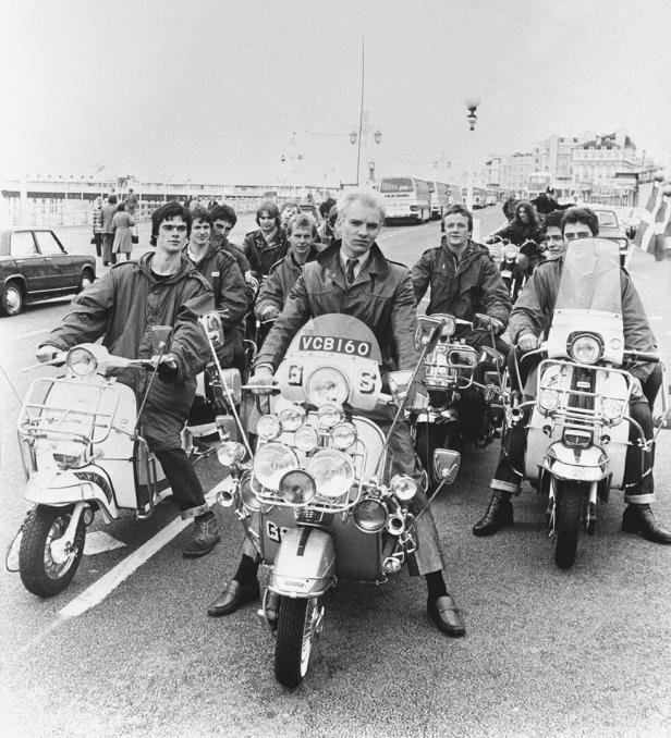 Eine Gruppe von Männern auf Motorrollern, möglicherweise Mods, auf einer Straße.