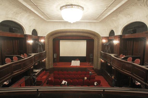 Blick auf die Bühne eines leeren Theaters mit rotem Teppich und roten Sitzen.