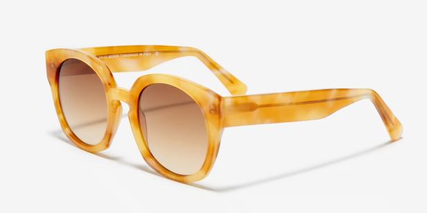 Eine gelb-braune Sonnenbrille mit Farbverlaufgläsern liegt auf einem weißen Hintergrund.