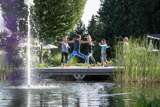 Mehrere Personen machen an einem Teich Yoga.