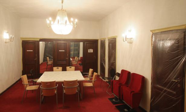 Ein Raum mit einem Tisch, Stühlen, einem Kronleuchter und abgedeckten Türen.
