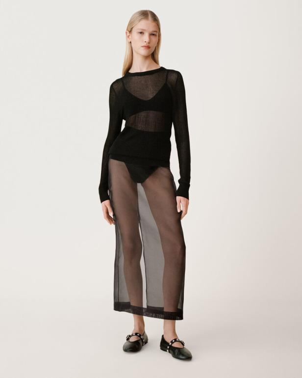 Eine Frau mit blonden Haaren trägt ein schwarzes, transparentes Kleid und Ballerinas.