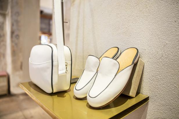 Eine weiße Handtasche und ein Paar weiße Lederschuhe von Maßschuhe Scheer stehen auf einem Tisch.