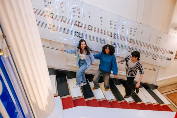 Drei Kinder gehen eine Treppe in einem Gebäude hinunter, die wie die Tasten eines Klaviers aussehen.