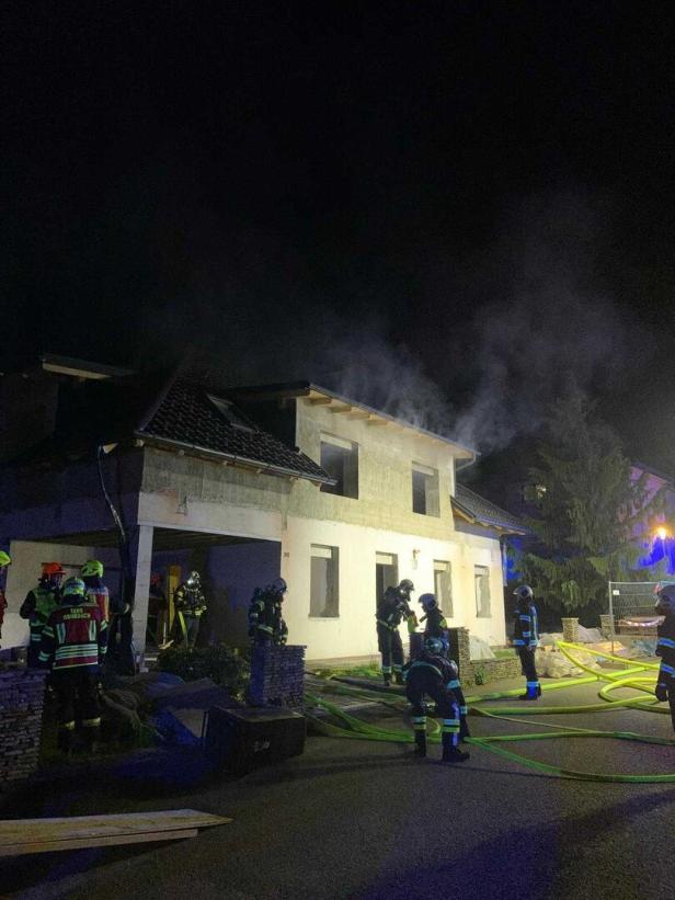 Feuerwehrleute stehen vor einem Haus, aus dem Rauch dringt.