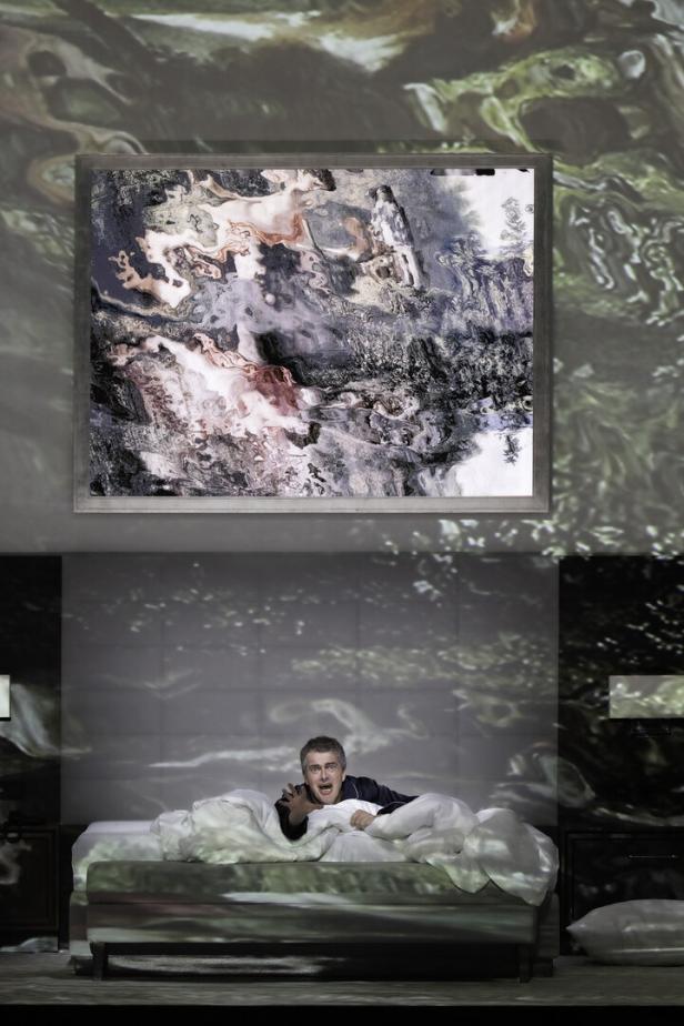 Ein Mann liegt auf einem Bett und schreckt auf, während abstrakte Bilder projiziert werden.