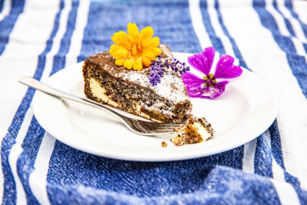 Ein Stück Mohnkuchen mit Puderzucker und Blüten auf einem Teller.