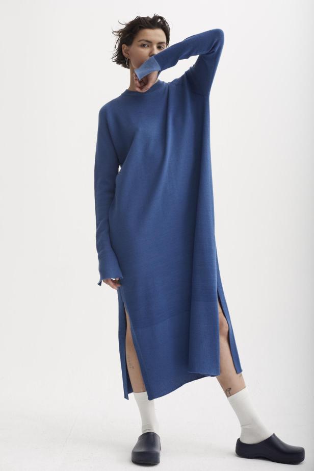 Eine Frau in einem langen, blauen Strickkleid mit Schlitzen und weißen Socken.