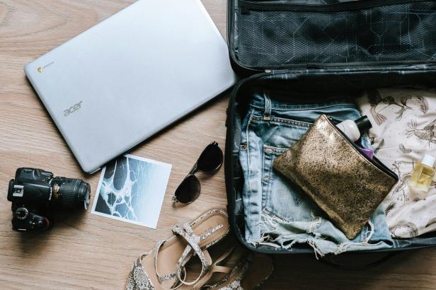 Ein offener Koffer, um den Laptop, Kamera, Sonnenbrille und Postkarte liegt.