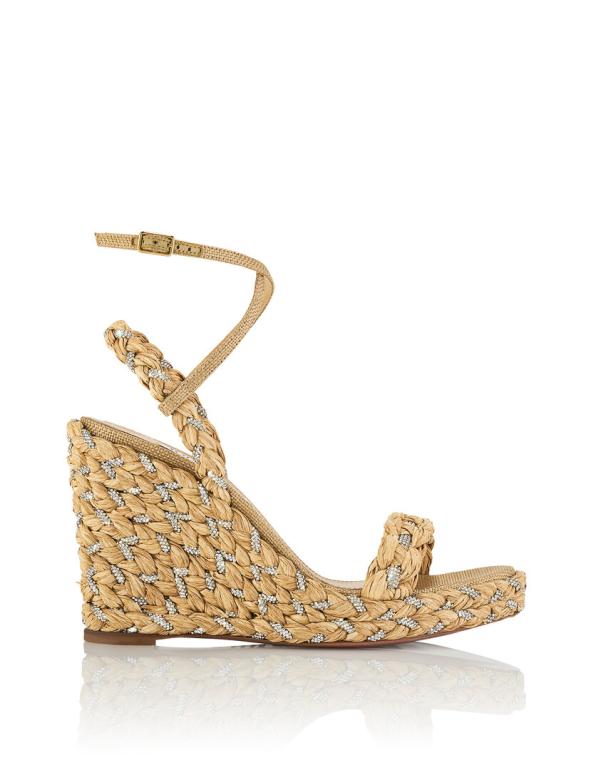 Ein goldfarbener Keilabsatz-Sandal mit geflochtenen Details und Strasssteinen steht auf einem weißen Hintergrund.
