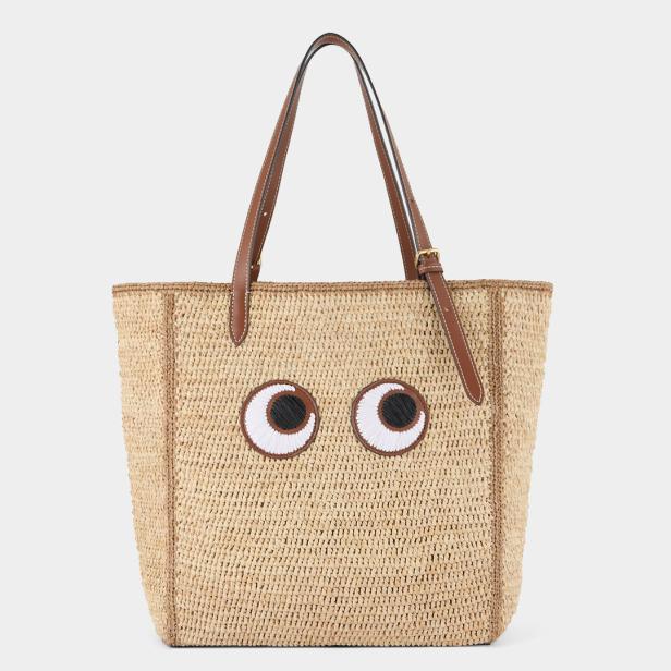 Eine Strohtasche mit aufgenähten, großen Augen und braunen Ledergriffen.