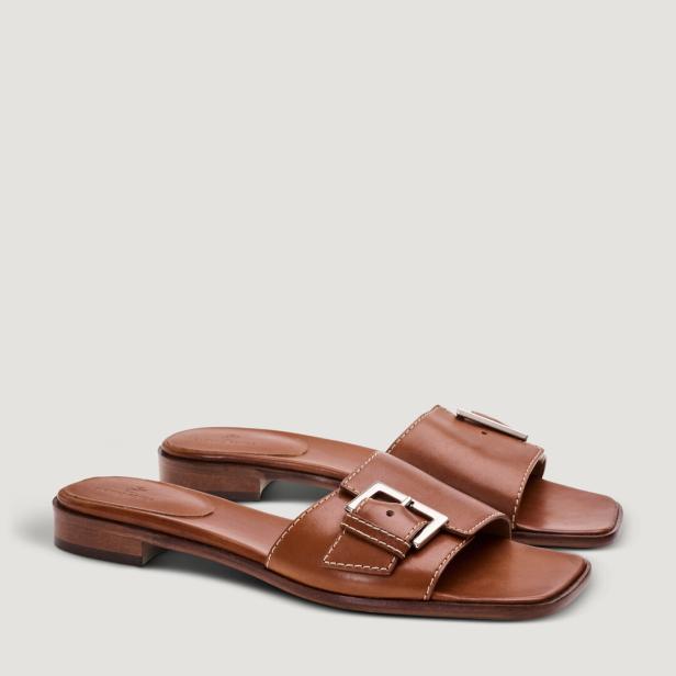 Ein Paar braune Ledersandalen mit silbernen Schnallen stehen auf einem hellen Hintergrund.