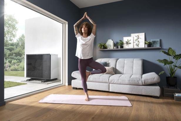 Eine Frau praktiziert Yoga in ihrem Wohnzimmer, umgeben von Pflanzen und einem ruhigen, einladenden Ambiente.