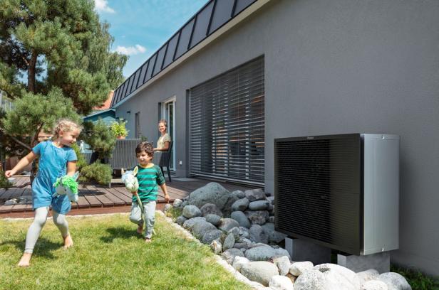 Zwei Kinder genießen das Spielen im Garten, während eine Wärmepumpe beim Haus im Hintergrund sichtbar ist.