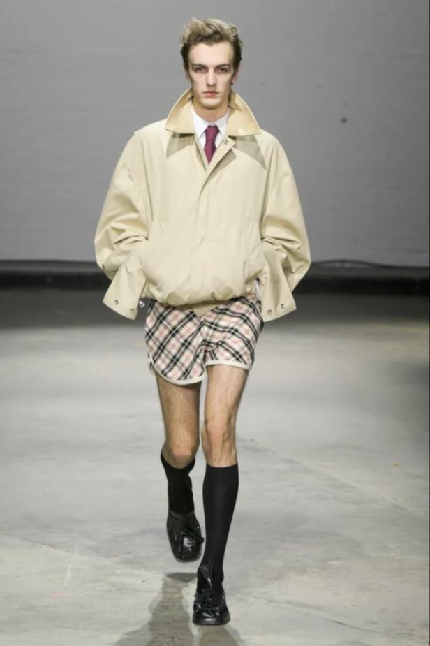 Ein Mann in Shorts, Jacke und Kniestrümpfen läuft auf einem Laufsteg.