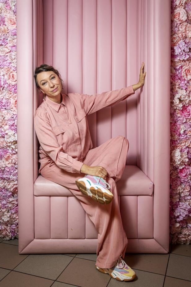Ursula Strauss posiert in einem rosa Anzug vor einem Blumenhintergrund.