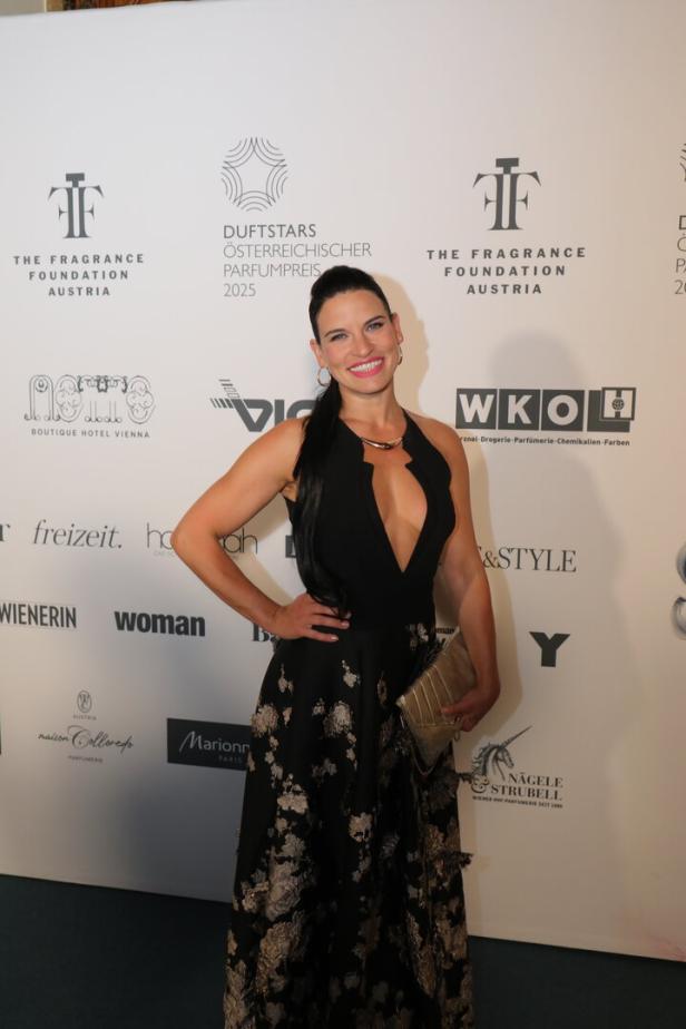 Eine Frau in Abendgarderobe posiert vor einer Wand mit Sponsorenlogos.