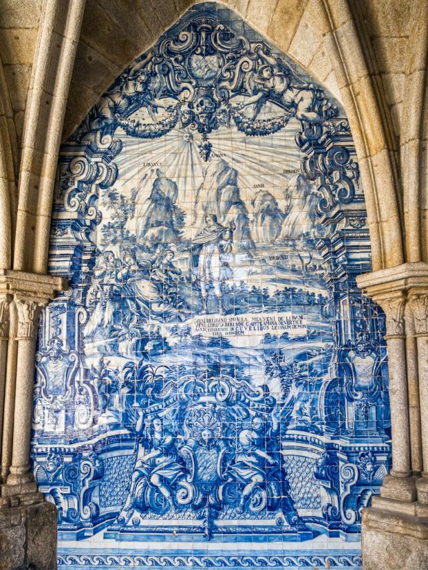 Eine blau-weiße Azulejo-Wandmalerei unter einem steinernen Torbogen zeigt biblische Szenen und lateinische Inschriften.
